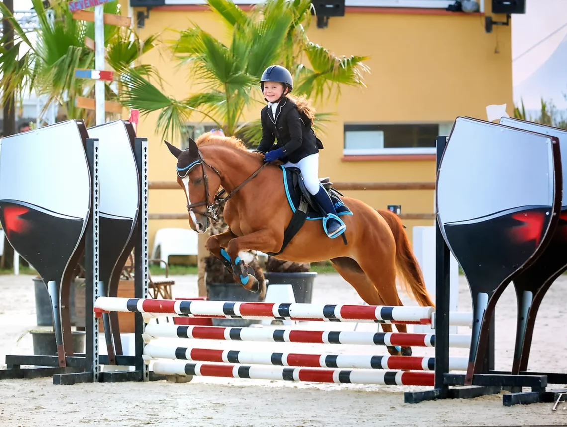 Jeune cavalière sur son poney franchissant un obstacle en concours
